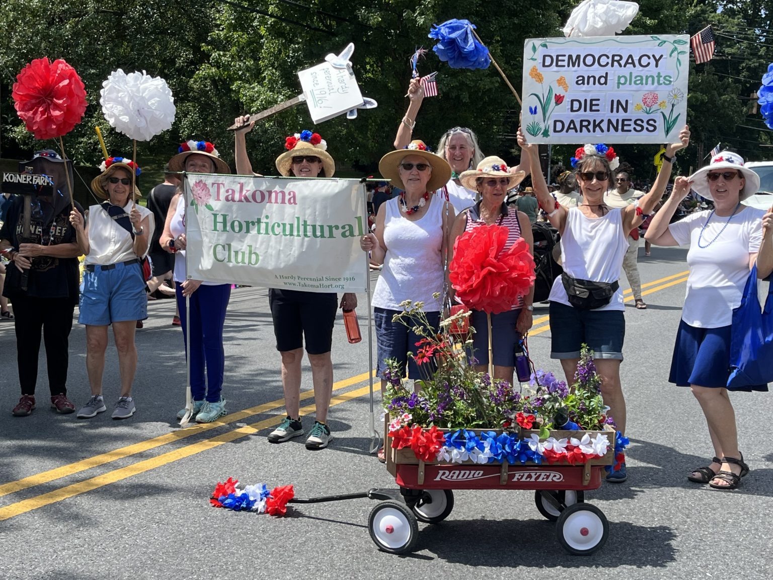 Club members marching in the 4th of July parade with a sign that says: Democracy and Plants Die in Darkness".
